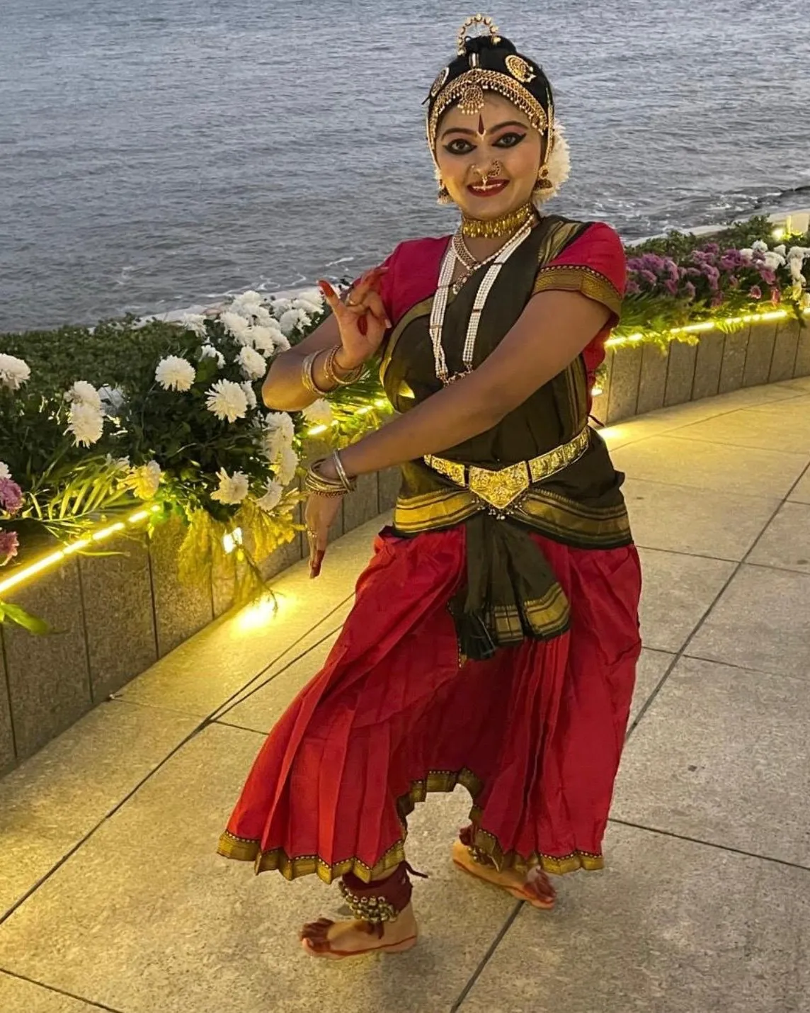 Binni Patel performing Bharatanatyam outdoors by the water, in full costume and makeup.