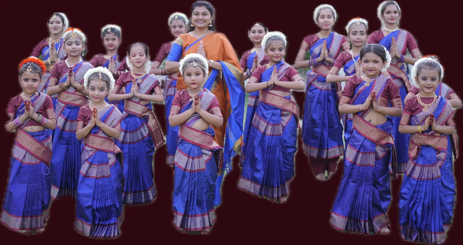 Sixteen students in blue and maroon Bharatanatyam costume standing with Binni Patel, hands folded in namaskaram.
