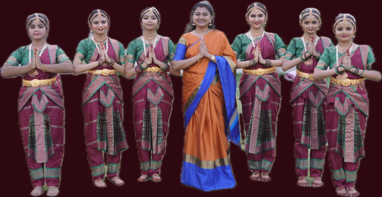 Seven students in green and maroon Bharatanatyam costume standing with Binni Patel, all with hands folded in namaskaram.